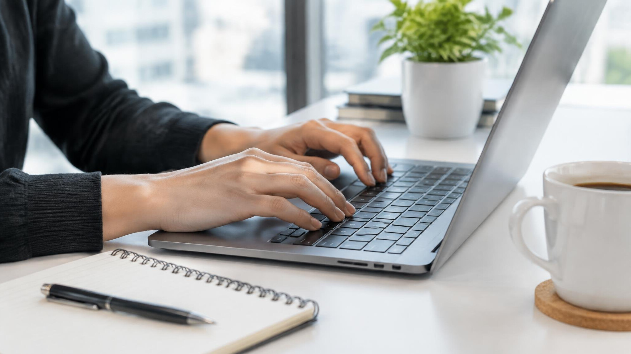 Close-up of hands typing on a laptop keyboard at a modern office desk